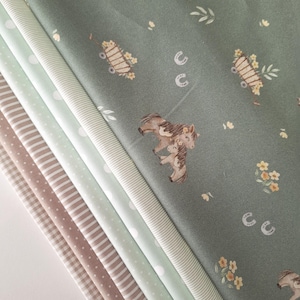 Könnte beinhalten: Ein Stapel verschiedener Stoffe mit Pferdemotiv. Der obere Stoff ist salbeigrün mit Pferdeillustrationen, Blumenwagen und Hufeisen. Weitere Stoffe sind weiße Punkte, Streifen und Vichy-Muster in Grün-, Weiß- und Brauntönen.