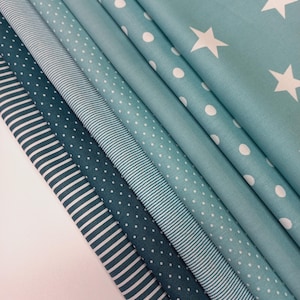 Könnte beinhalten: Ein Stapel verschiedener blauer Stoffe mit weißen Mustern. Die Muster umfassen Streifen, Punkte und Sterne. Die Stoffe reichen in den Farbtönen von Türkis bis Marineblau. Die Stoffe sind gefaltet und geschichtet, wodurch eine optisch ansprechende Darstellung entsteht.