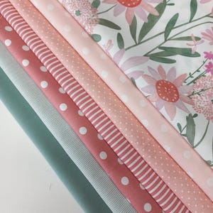 Könnte beinhalten: Ein Stapel von sieben Stoffproben in verschiedenen Rosatönen und Grün. Die oberste Probe hat einen weißen Hintergrund mit einem rosafarbenen Blumenmuster. Die restlichen Proben haben verschiedene Muster, darunter Punkte, Streifen und einfarbige Farben.