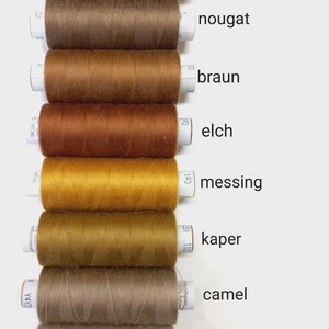 Könnte beinhalten: Neun Garnrollen in verschiedenen Brauntönen, von dunkel Schokoladenbraun bis hell Beige. Die Rollen sind mit deutschen Farbnamen beschriftet: schokoladenbraun, nougat, braun, elch, messing, kaper, camel und dunkelbeige.
