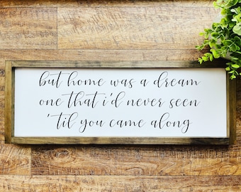 May include: White wooden sign with black calligraphy that reads "but home was a dream one that i'd never seen 'til you came along"