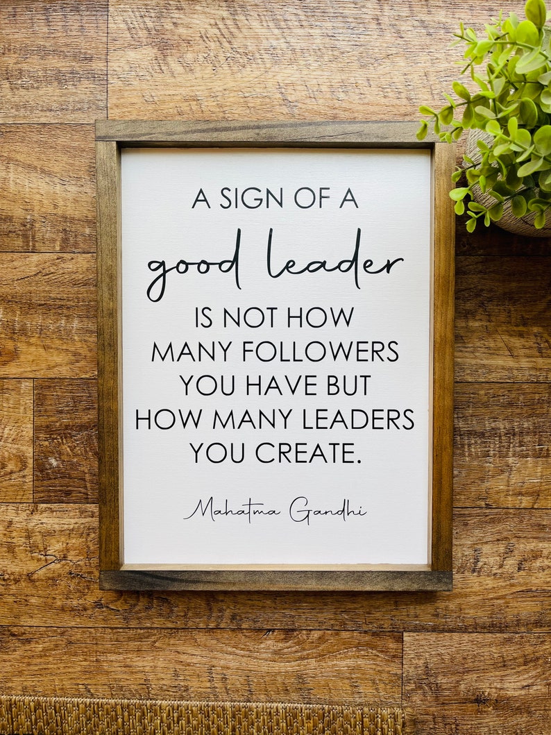 May include: A framed sign with a white background and black text that reads "A sign of a good leader is not how many followers you have but how many leaders you create. Mahatma Gandhi".