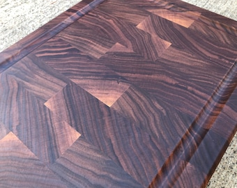 Puede incluir: Una tabla de cortar de madera marrón oscuro grande con un patrón de espiga. La tabla tiene un borde elevado alrededor del perímetro.