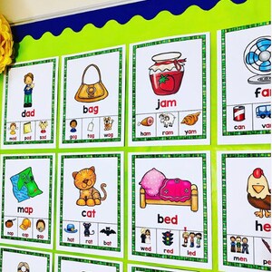 May include: A green noticeboard with colourful flashcards featuring words and pictures. The words include "dad", "bag", "jam", "can", "map", "cat", "bed", "fan", and "hen".