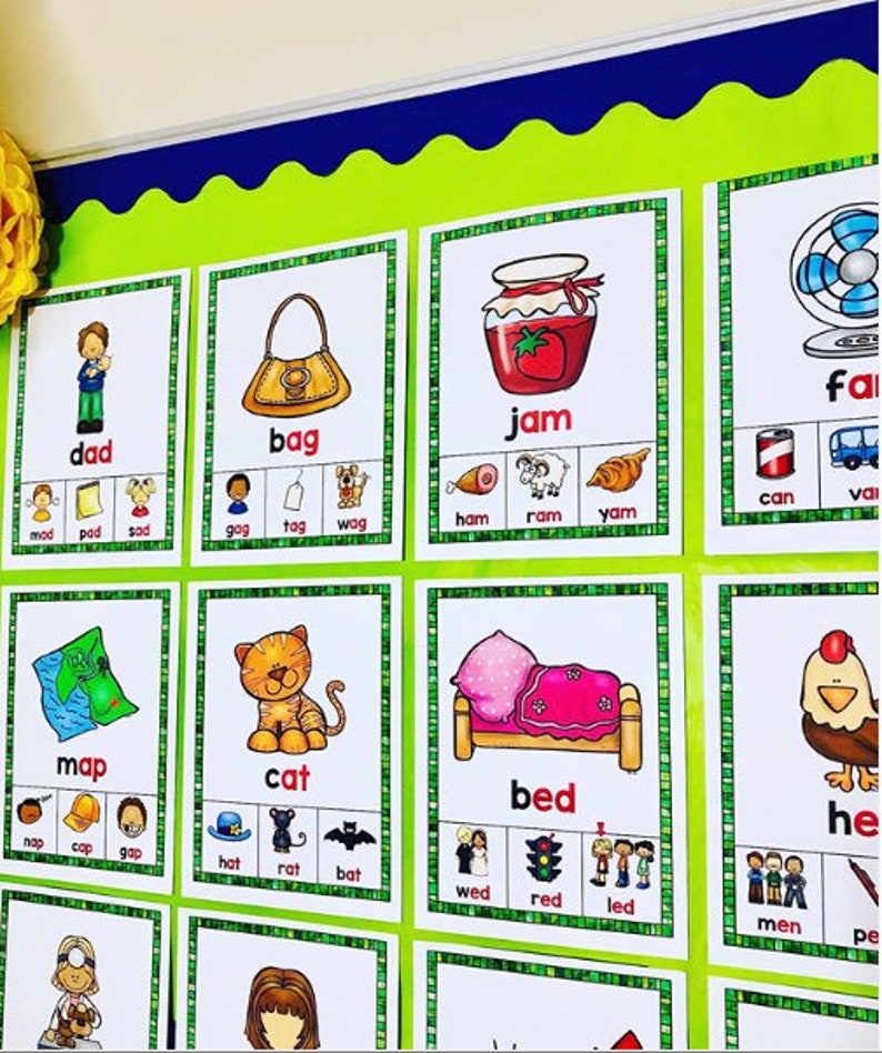 May include: A green noticeboard with colourful flashcards featuring words and pictures. The words include "dad", "bag", "jam", "can", "map", "cat", "bed", "fan", and "hen".