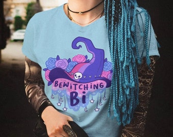 May include: A light blue t-shirt with a graphic of a witch's hat with flowers and the text "Bewitching Bi" in pink and blue lettering.