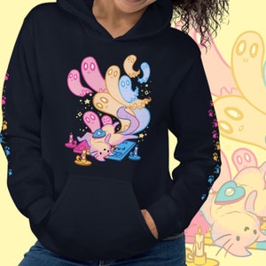 Peut inclure: Un sweat-shirt &agrave; capuche noir avec une illustration color&eacute;e d'un chat entour&eacute; de fant&ocirc;mes. Le chat porte un chapeau bleu et tient un instrument de musique. Le sweat-shirt a une poche sur le devant et une capuche &agrave; cordon.