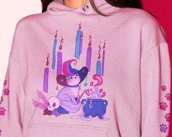May include: A lavender hoodie with a graphic of a cat wearing a witch hat and holding a wand. The cat is surrounded by candles and a cauldron. The sleeves of the hoodie have a repeating paw print design.