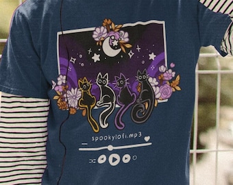 May include: A navy blue t-shirt with a graphic of three black cats sitting in front of a crescent moon and stars. The graphic also includes flowers and the text "spookylofi.mp3" with a music player icon.