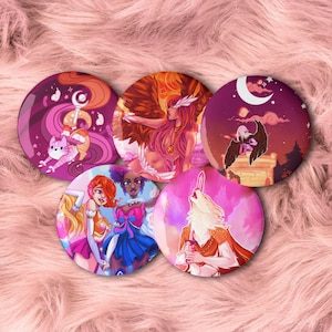 Peut inclure: Cinq badges ronds et colorés avec des illustrations d'art fantastique. Les motifs présentent des personnages aux longs cheveux, des ailes et des éléments célestes dans des tons de rose, de violet, d'orange et de bleu. Les badges sont disposés sur une surface rose et floue.