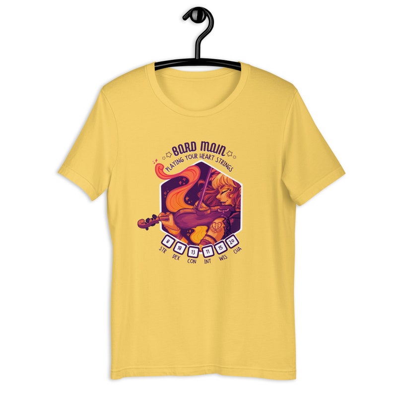 May include: Yellow t-shirt with a graphic of a woman playing a violin. The graphic is in a hexagon shape with the text "Bard Main" and "Playing Your Heart Strings". The hexagon also has a D&D character sheet with stats like STR, DEX, CON, INT, WIS, and CHA.