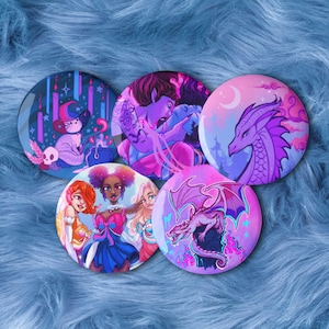 May include: Set of five round buttons with fantasy art designs. The buttons feature illustrations of a cat in a witch hat, figures with tattoos, a dragon, and a group of women. The color palette includes shades of purple, pink, and blue.