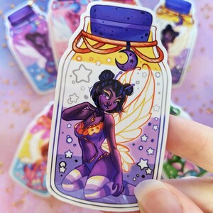 May include: A sticker of a glass jar with a purple, yellow, and white design. Inside the jar is a fairy with purple wings and a yellow and purple outfit. The fairy is holding a crescent moon.