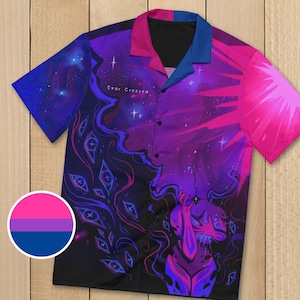May include: A short-sleeved button-down shirt with a vibrant cosmic design in shades of purple, pink, and blue. The shirt features a celestial illustration with the text "Star Crossed" and a circular bisexual pride flag emblem.