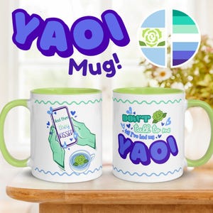 May include: Two white ceramic mugs with green interiors and handles. One mug features the text "And then they KISSED" and a phone graphic. The other mug says "DON'T talk to me till I've had my YAOI". Both mugs have a blue and green design.