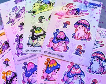 May include: A collection of colorful stickers featuring whimsical illustrations of bunnies and mushroom characters. The stickers have a variety of designs, including bunnies with mushroom caps and mushroom-shaped creatures. The text "Bun Shrooms Evocaitart" is visible.