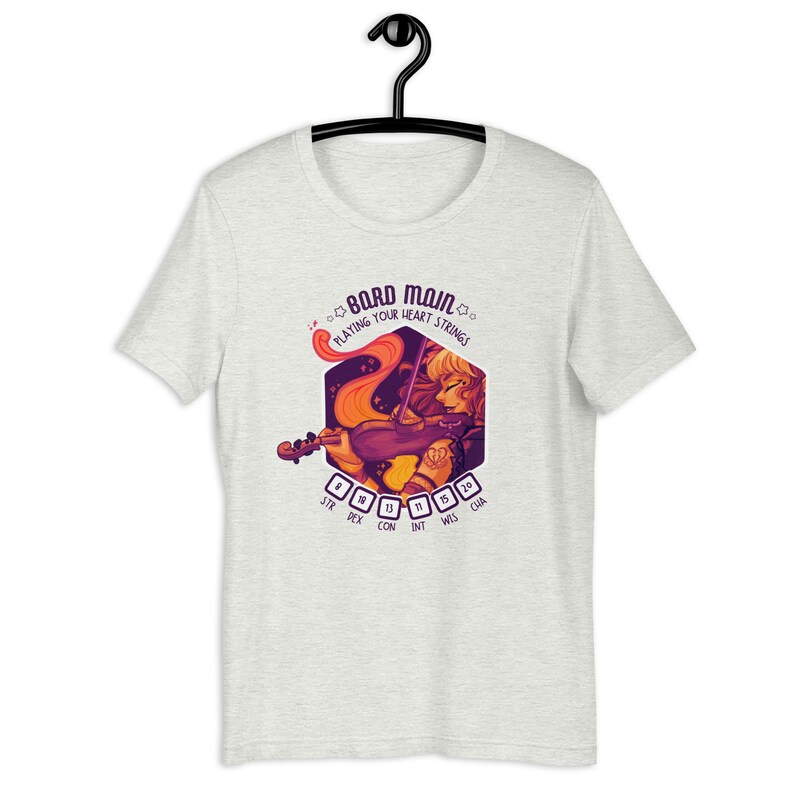 May include: A heather grey t-shirt with a purple and orange illustration of a bard playing a violin. The illustration is inside a hexagon with the text "Bard Main" and "Playing Your Heart Strings" above the illustration. The text "STR DEX CON INT WIS CHA" is below the illustration.