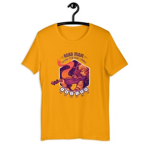 May include: A yellow t-shirt with a graphic of a woman playing a violin. The graphic is in a hexagonal shape with the text "Bard Main" and "Playing Your Heart Strings" above the image. The text "STR DEX CON INT WIS CHA" is below the image with dice numbers next to each word.