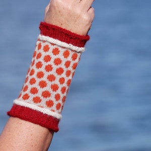 Peut inclure: Manchon tricoté avec un motif à pois orange et blanc. Le manchon a des poignets rouges et une bande blanche. L'arrière-plan est un bleu flou.