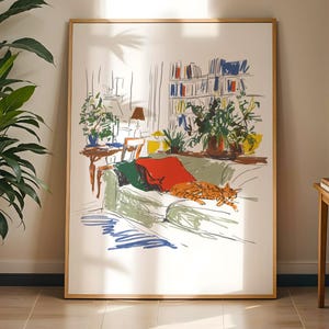 May include: A framed art print shows a living room with a green sofa, a red blanket, and an orange cat. The artwork includes a bookshelf, plants, and a table with a lamp. A large potted plant and a small side table with a plant are also visible.