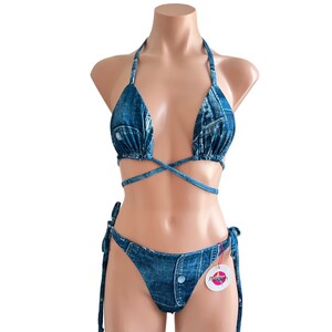 May include: A denim blue bikini top and bottom with a criss-cross tie at the top and a button detail on the bottom. The bikini is made of a stretchy fabric and has a faded denim look.