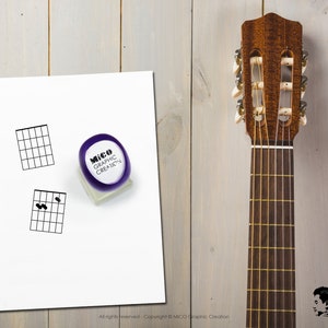May include: A white sheet of paper with two guitar chord diagrams printed on it. A purple rubber stamp with the text "Mico Graphic Creation" is on the paper. A brown wooden guitar neck is on the right side of the image.