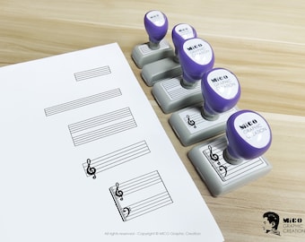May include: A collection of music-themed stamps with purple handles and gray bases, alongside a sheet of paper with printed musical staff lines and clef symbols. The stamps are labeled "MICO GRAPHIC CREATION". The image is on a wooden surface.