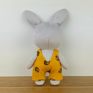 May include: A grey plush bunny wearing yellow dungarees with a black bee pattern.