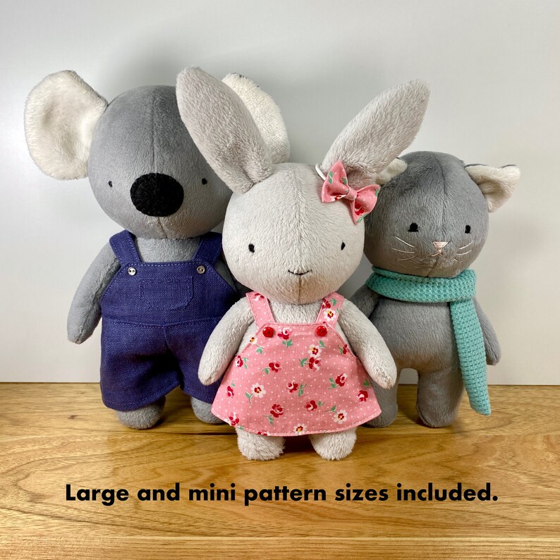 K&ouml;nnte beinhalten: Drei Pl&uuml;schtiere: ein grauer Koala in blauer Latzhose, ein graues Kaninchen in einem rosa Blumenkleid und eine graue Katze mit einem t&uuml;rkisfarbenen Schal.  Gro&szlig;e und kleine Mustergr&ouml;&szlig;en enthalten.