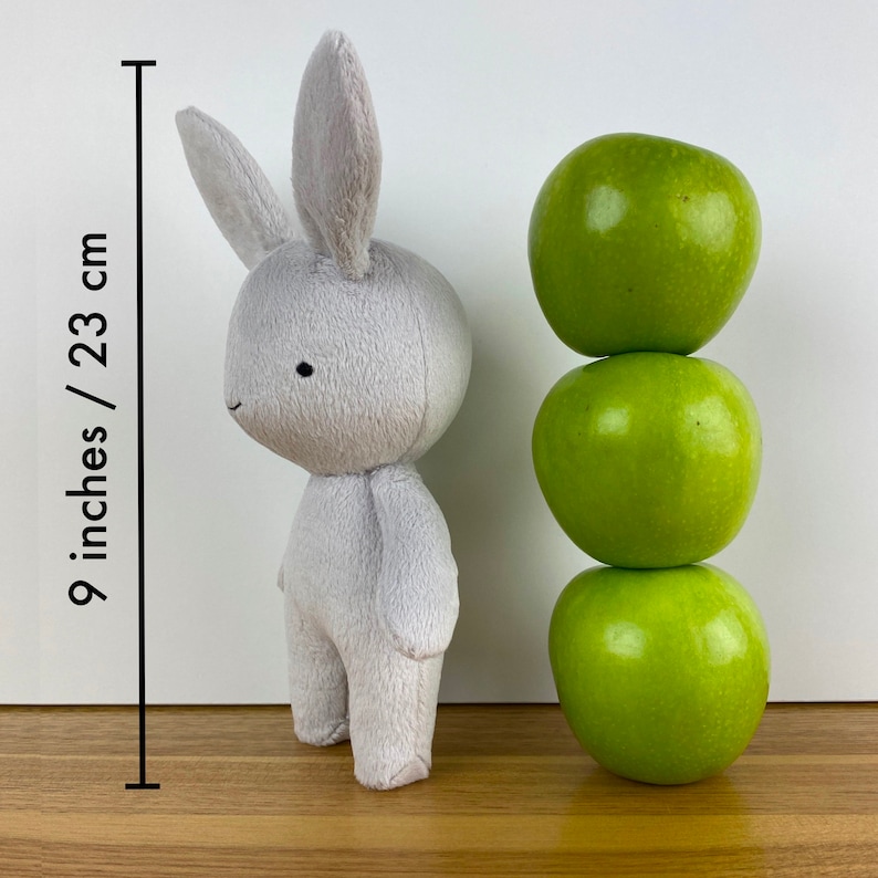 May include: A grey plush bunny rabbit toy standing 23 cm tall, next to a stack of three green apples.