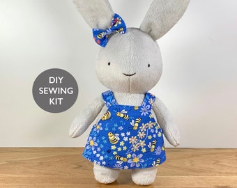 May include: DIY sewing kit featuring a plush gray bunny wearing a blue dress with a bee and flower pattern. The bunny has a small bow on its head.
