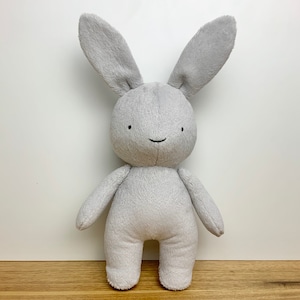 May include: A grey plush bunny toy with a simple, smiling face. The bunny has long ears and a soft, fluffy texture.