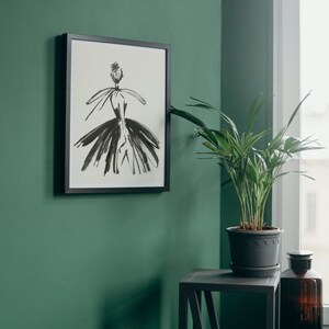 May include: A framed black and white illustration of a woman in a dress, hanging on a green wall. A potted plant sits on a black side table next to a brown glass bottle.