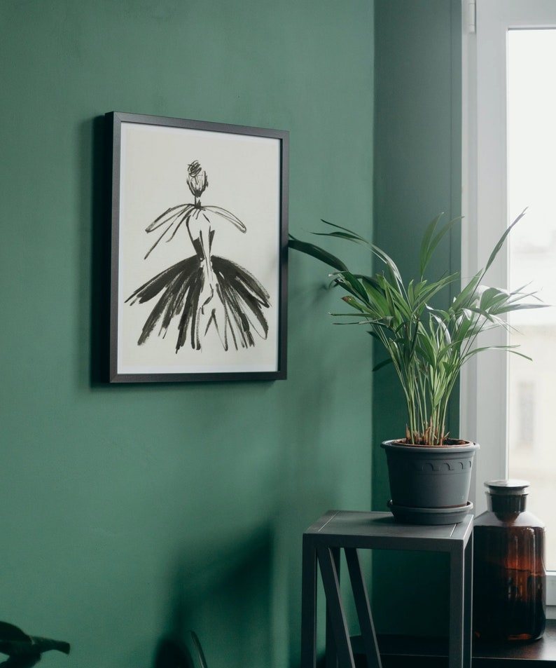 May include: A framed black and white illustration of a woman in a dress, hanging on a green wall. A potted plant sits on a black side table next to a brown glass bottle.