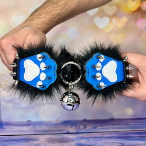 May include: A blue leather collar with black fur trim and silver paw prints. The collar has a silver bell attached to it.