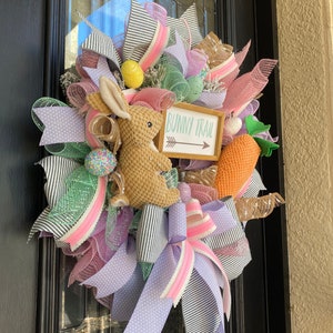 May include: Easter wreath with a woven bunny, decorative eggs, and a carrot. The wreath features ribbons in pink, lavender, green, and black and white stripes. A sign reads "Bunny Trail" with an arrow.