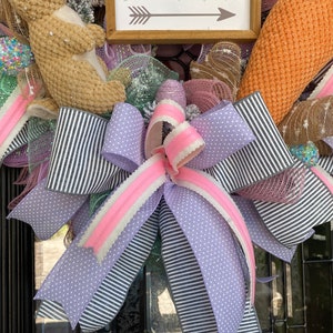 May include: Easter wreath with a brown bunny, carrot, and decorative ribbons. The wreath features a sign that reads "Bunny Trail" with an arrow. Ribbons are black and white striped, lavender polka dot, and pink.
