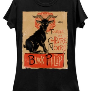 May include: Black t-shirt featuring a vintage-style graphic of a black goat with large horns. The design includes the text "Tourn&eacute;e de la Ch&egrave;vre Noire" and "Black Phillip" in red and black fonts, set against a tan background.