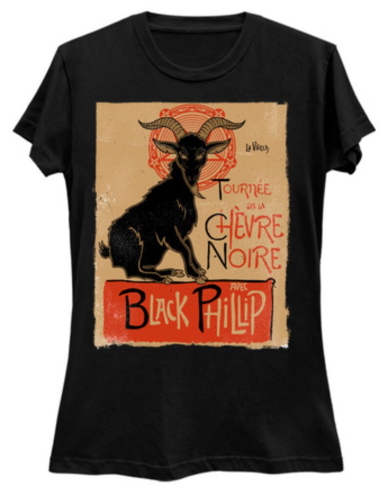 May include: Black t-shirt featuring a vintage-style graphic of a black goat with large horns. The design includes the text "Tourn&eacute;e de la Ch&egrave;vre Noire" and "Black Phillip" in red and black fonts, set against a tan background.
