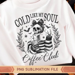 May include: A white sweatshirt with a black and white graphic design of a skeleton holding a cup of coffee. The text on the graphic says "Cold Like My Soul Coffee Club".