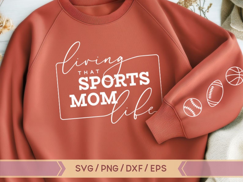 Op de afbeelding: Een roestkleurig sweatshirt met de tekst "Living that Sports Mom Life" in wit. Het sweatshirt heeft een witte omtrek van een rechthoek rond de tekst. De mouw van het sweatshirt heeft witte contouren van een honkbal, voetbal en basketbal.