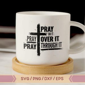 May include: White ceramic mug with a black cross and the text "PRAY ON IT PRAY OVER IT PRAY THROUGH IT". The mug is sitting on a wooden coaster.