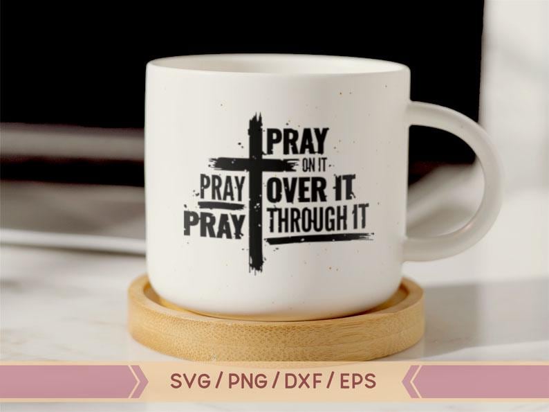 May include: White ceramic mug with a black cross and the text "PRAY ON IT PRAY OVER IT PRAY THROUGH IT". The mug is sitting on a wooden coaster.