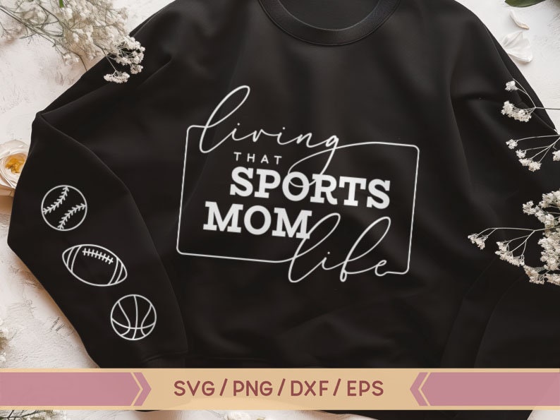 Op de afbeelding: Zwart sweatshirt met witte tekst die "Living that Sports Mom Life" luidt. Het sweatshirt heeft een witte baseball, voetbal en basketbal afbeelding op de mouw.