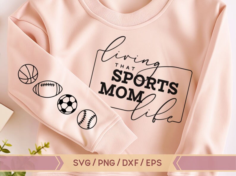 Op de afbeelding: Roze sweatshirt met de tekst "Living that Sports Mom Life" in zwarte cursieve letters. De mouw heeft een rij zwarte sportpictogrammen: een basketbal, een voetbal, een voetbal en een honkbal.