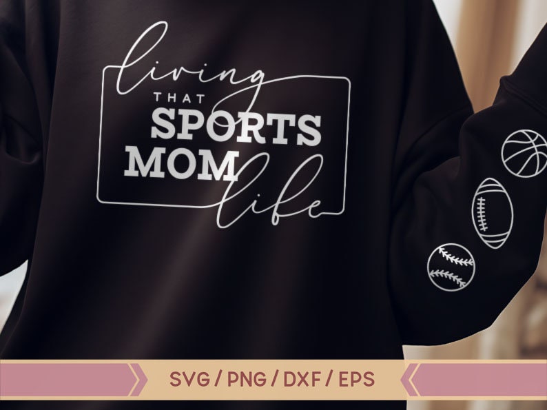 Op de afbeelding: Zwart sweatshirt met witte tekst die "Living that Sports Mom Life" luidt. Het sweatshirt heeft witte contouren van sportballen op de mouw.