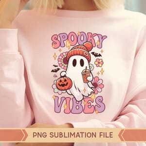 May include: Pink sweatshirt with a graphic of a ghost wearing a hat and holding a pumpkin and a cup. The text "Spooky Vibes" is printed on the sweatshirt.