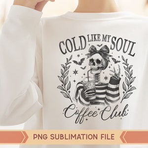 May include: A white t-shirt with a black and white graphic design featuring a skeleton holding a cup of coffee. The graphic says "Cold Like My Soul Coffee Club".