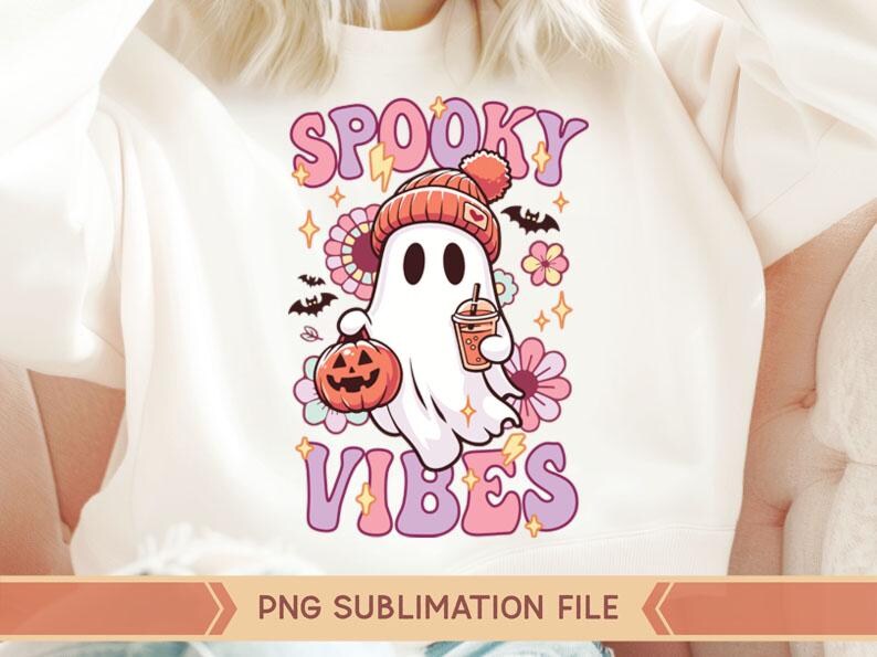 May include: A white t-shirt with a pink and purple graphic design featuring a cartoon ghost wearing a hat and holding a pumpkin and a cup. The text "Spooky Vibes" is written in pink and purple letters.