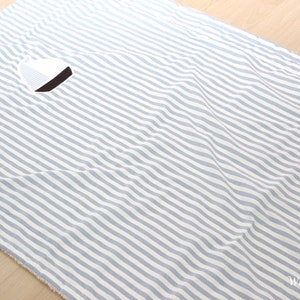 Könnte beinhalten: Ein weiß- und hellblauer gestreifter Stoff mit einem kleinen weißen und schwarzen Kreis in der Mitte. Der Stoff hat eine weiche, flauschige Textur.